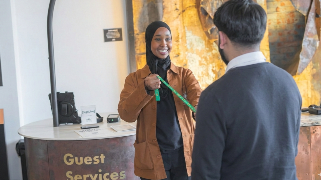 Smiling lady offers sunflower lanyard to guest