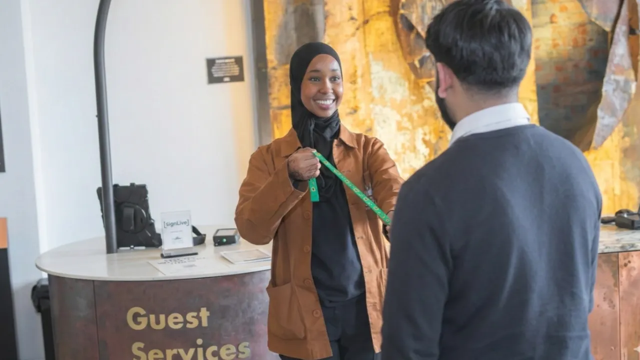 Smiling lady offers sunflower lanyard to guest