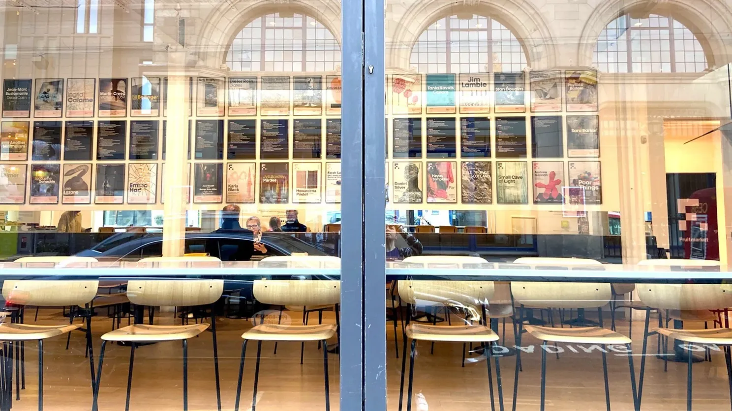 The Fruitmarket café seen from the street — well lit, with walls covered in previous exhibition posters, visitors enjoying the space