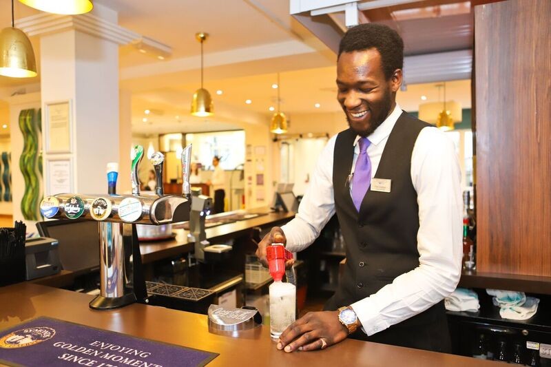 A smiling smartly dressed bartender pours a drink