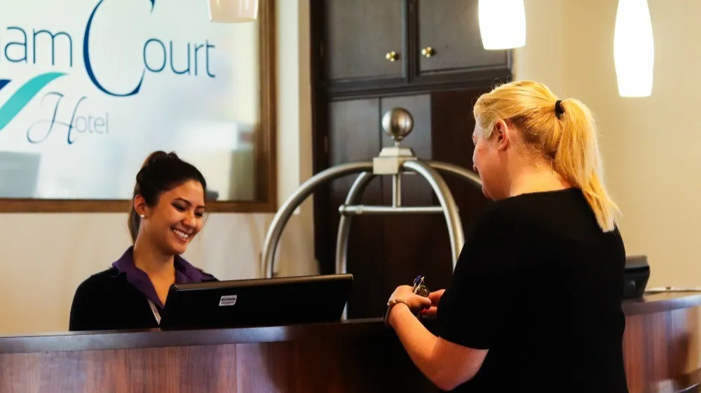 A young lady at a reception desk greets her guest with a genuine smile at Marsham Court Hotel