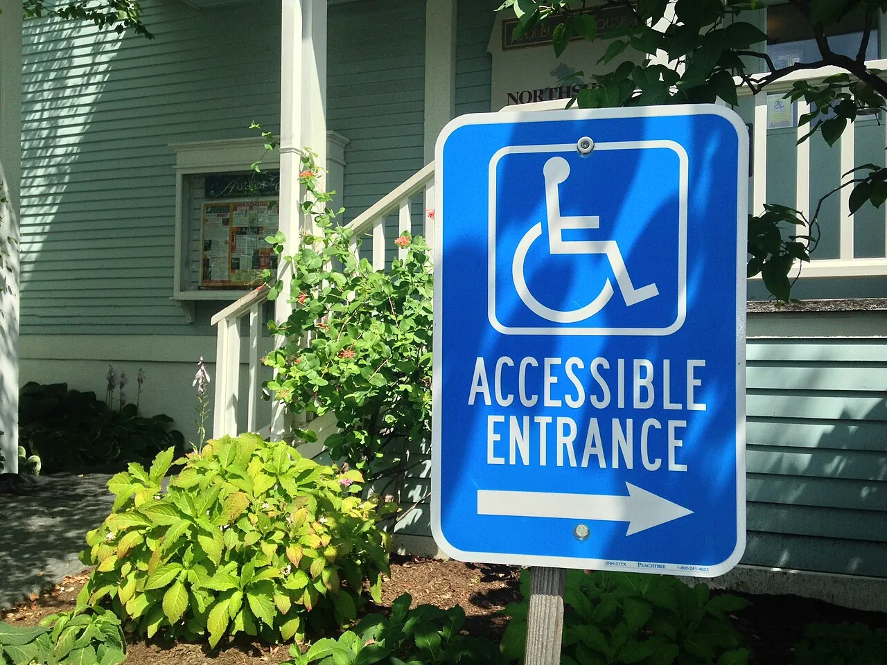 Blue sign with the wheelchair symbol reading "Accessible entrance" and an arrow pointing right