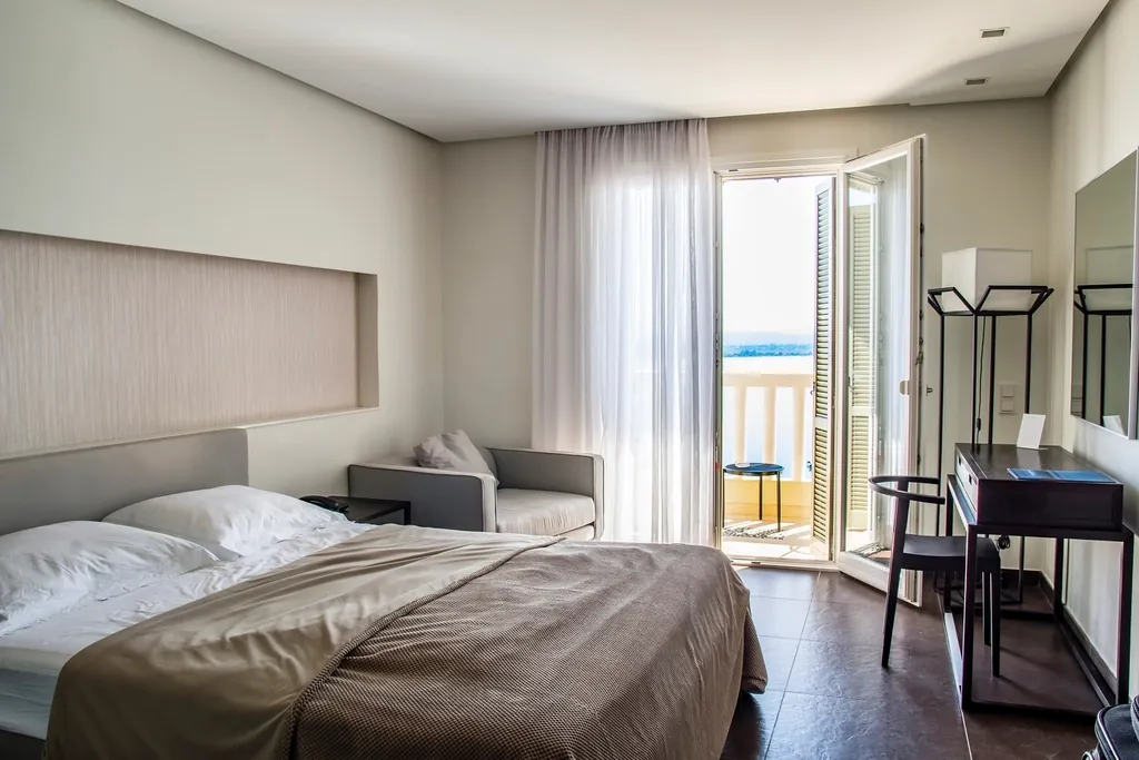 Bright bedroom with a large bed, a desk and glass doors opening onto a balcony